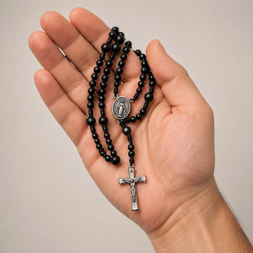 Black Compact Everyday Rosary resting in an adult hand to show its bead, medal, and crucifix scale.