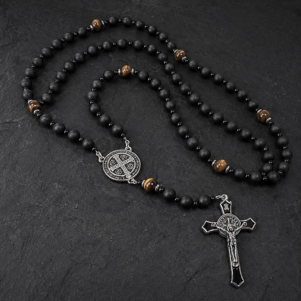St. Benedict five-decade rosary with matte black onyx beads, tiger eye accents, a silver-tone medal, and a black enamel crucifix on dark stone.