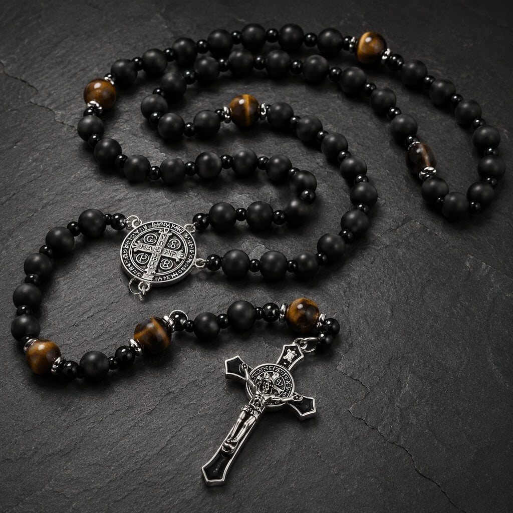 Black onyx and tiger eye St. Benedict rosary arranged on dark stone in a restrained church-inspired setting.