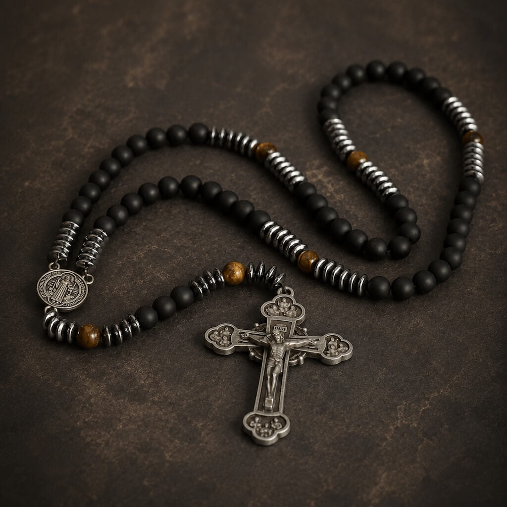 Black glass and tiger eye St. Benedict rosary arranged with its medal and ornate antiqued crucifix on a dark stone background.